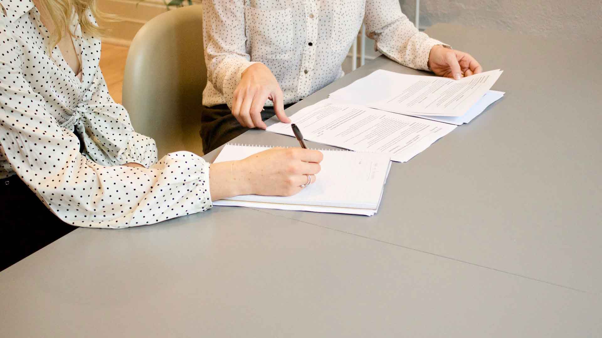 Dos mujeres en una oficina firmando y revisando un par de documentos